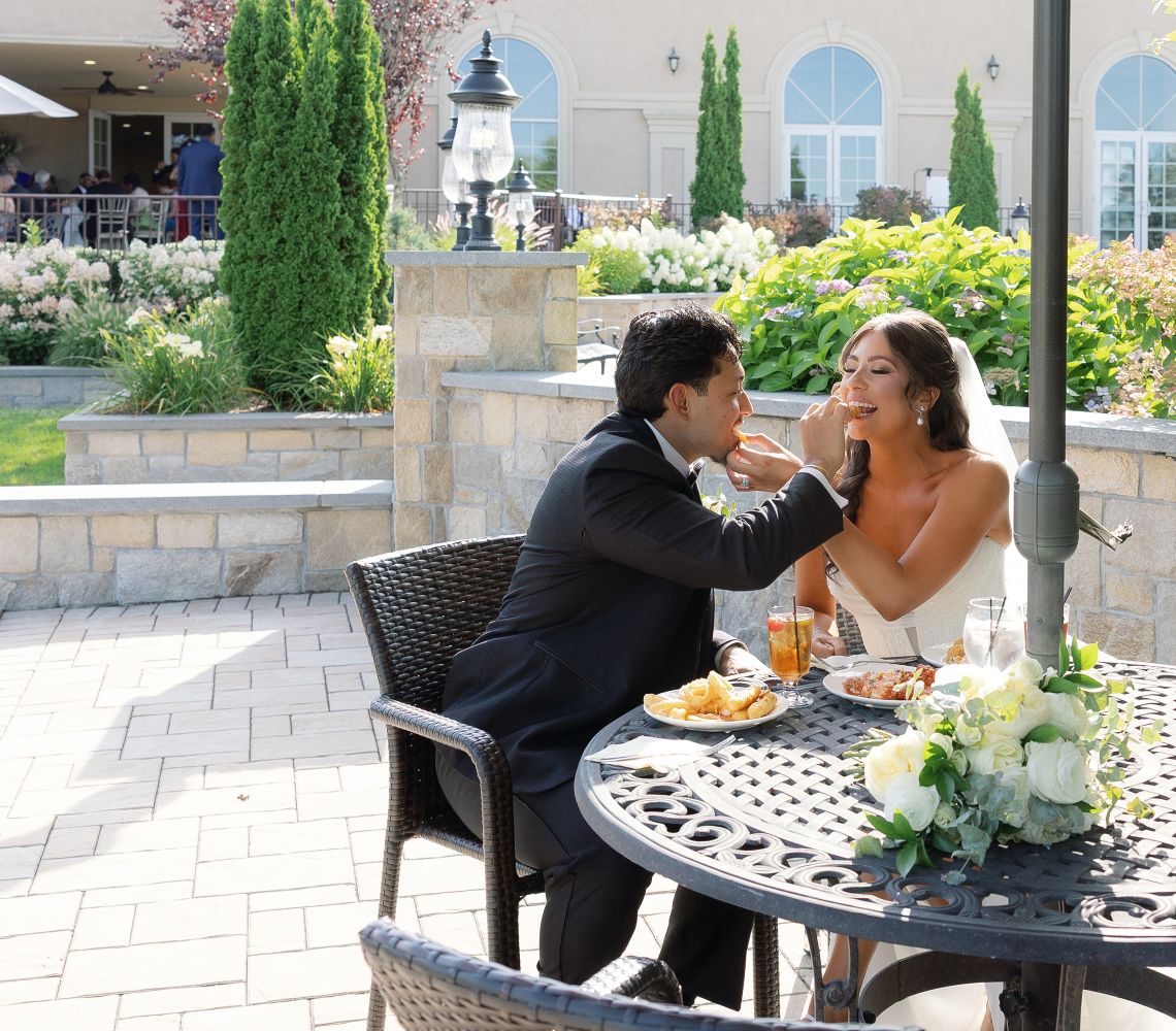 a bride and a groom feeding each other outside on the aria patio