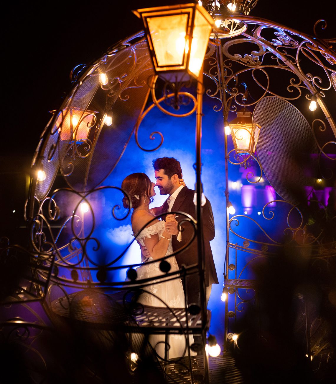 a bride and groom dancing outside at night in a metal wire carriage with blue lights in the background
