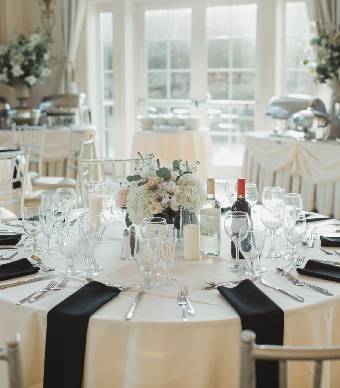 a table set for dinner with a white table cloth and black napkins at each seat