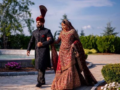 a bride and groom in traditional wedding attire walking outside on aria grounds