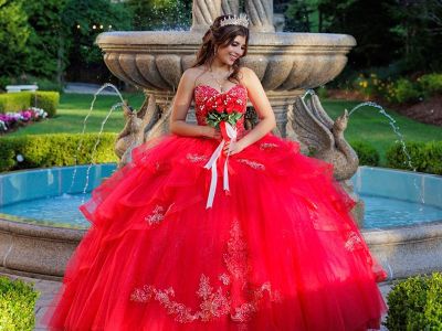 a teen girl posing for a picture in front of a fountain in a formal red dress